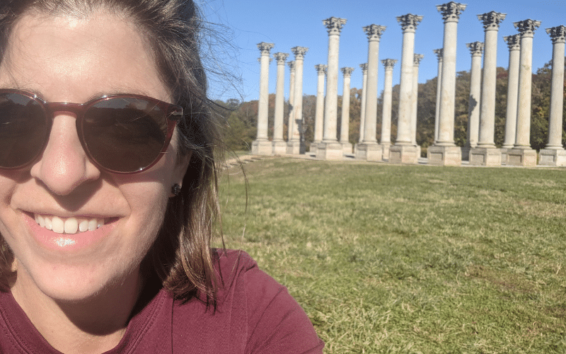 A selfie of Karina wearing sunglasses in front of the National Capitol Columns, an arrangement of twenty-two Corinthian columns in an open meadow.