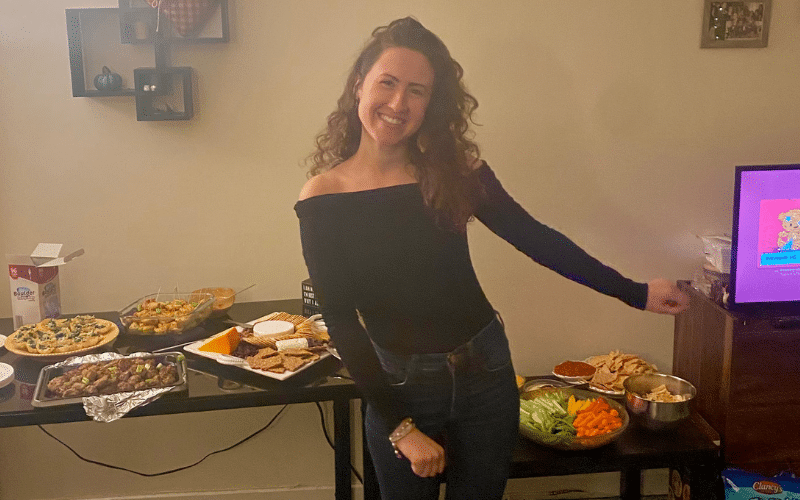 Rachel stands wearing a black top in front of two tables filled with platters of food.