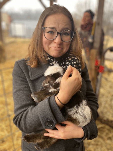 Hannah holds a fluffy baby goat and appears overcome with emotion. 