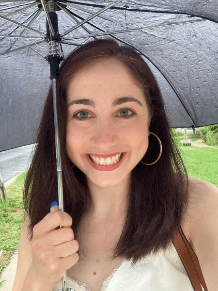 Becca holds a black umbrella and smiles