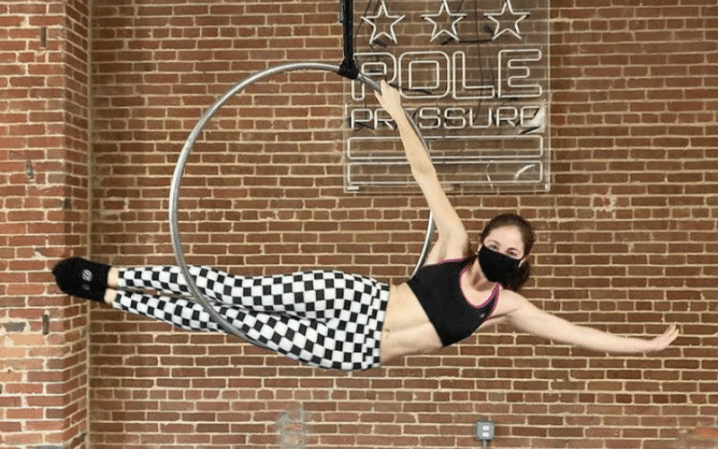 Becca, a white woman, poses horizontally in a suspended aerial hoop