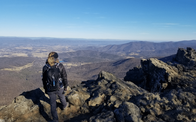 Sam wears hiking gear and stands overlooking a vast mountain range.