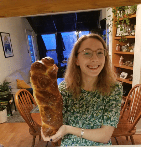 Sam holds up a large braided challah while standing in an apartment kitchen.