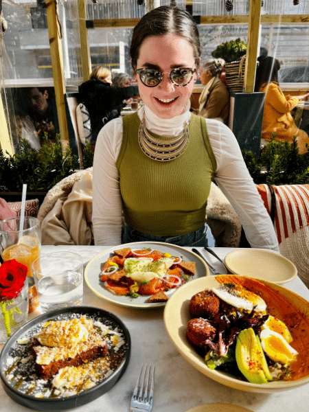 Becca sits at a table in a restaurant with a beautiful spread of colorful food on the table.