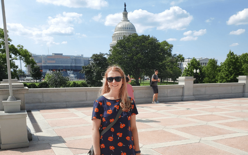 Paige, a white woman, stands in front of the US capitol on a sunny day.