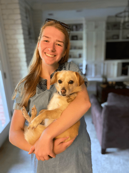 Paige smiles and cradles a small blonde dog in her arms. 