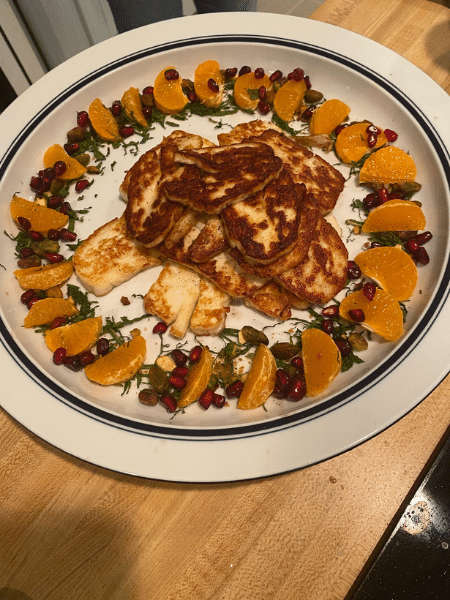 A dish that Jonathan prepared: A white plate with a heaping pile of golden fried haloumi cheese in the center by mandarin orange slices, pomegranate seeds, and a green herb. 