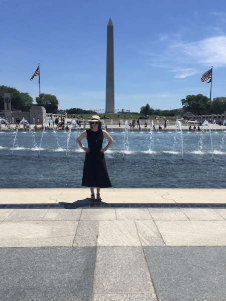 Glenna stands at the WWII memorial in front of a pond with fountains and with the Washington monument behind her.