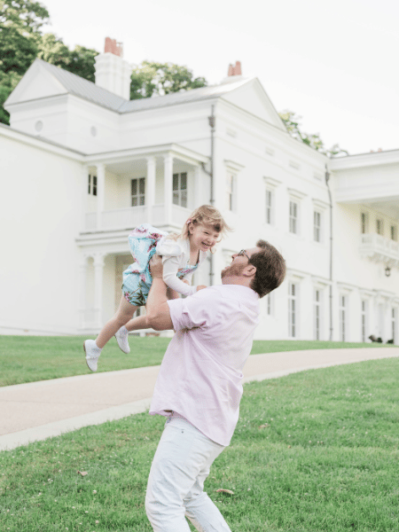 A picture of Josh holding his daughter in the air on an open field