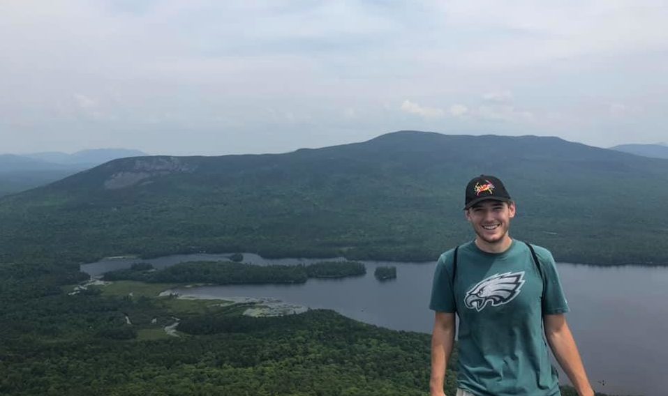 Samuel stands at the top of a mountain in a Philadelphia Eagles tee shirt.