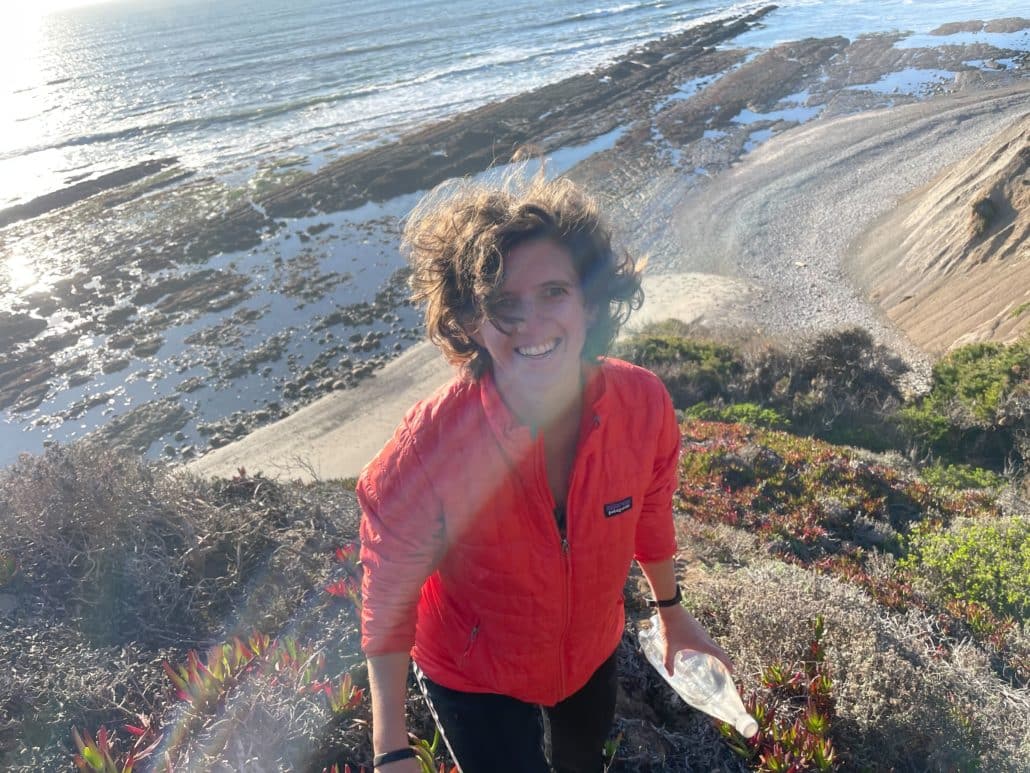 Caroline Kessler, wearing an orange Patagonia jacket, stands in a sunny tidal zone. 