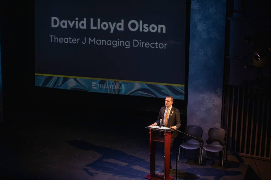 David Lloyd Olson speaks at a lectern onstage at Theater J. 