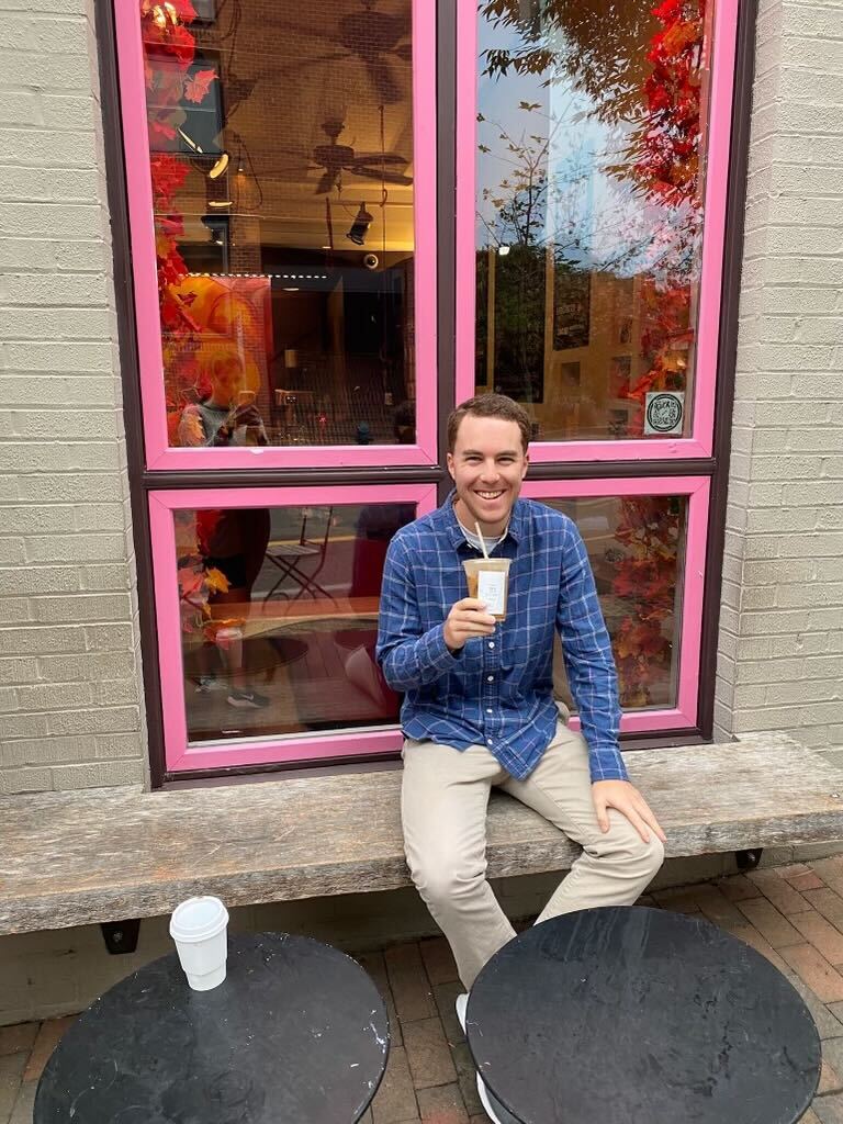 Corey of Capitol Grounds sits in a pink-rimmed windowsill with an iced drink. 