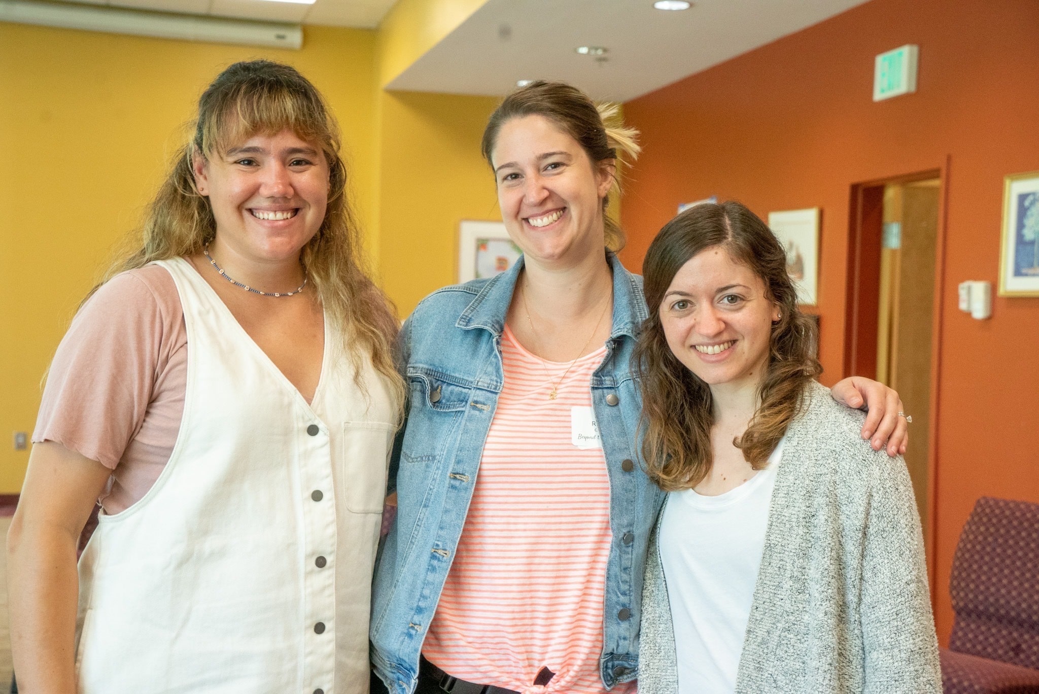 Rachel, Jackie, and Rabbi Ilana stand together and smile indoors. 