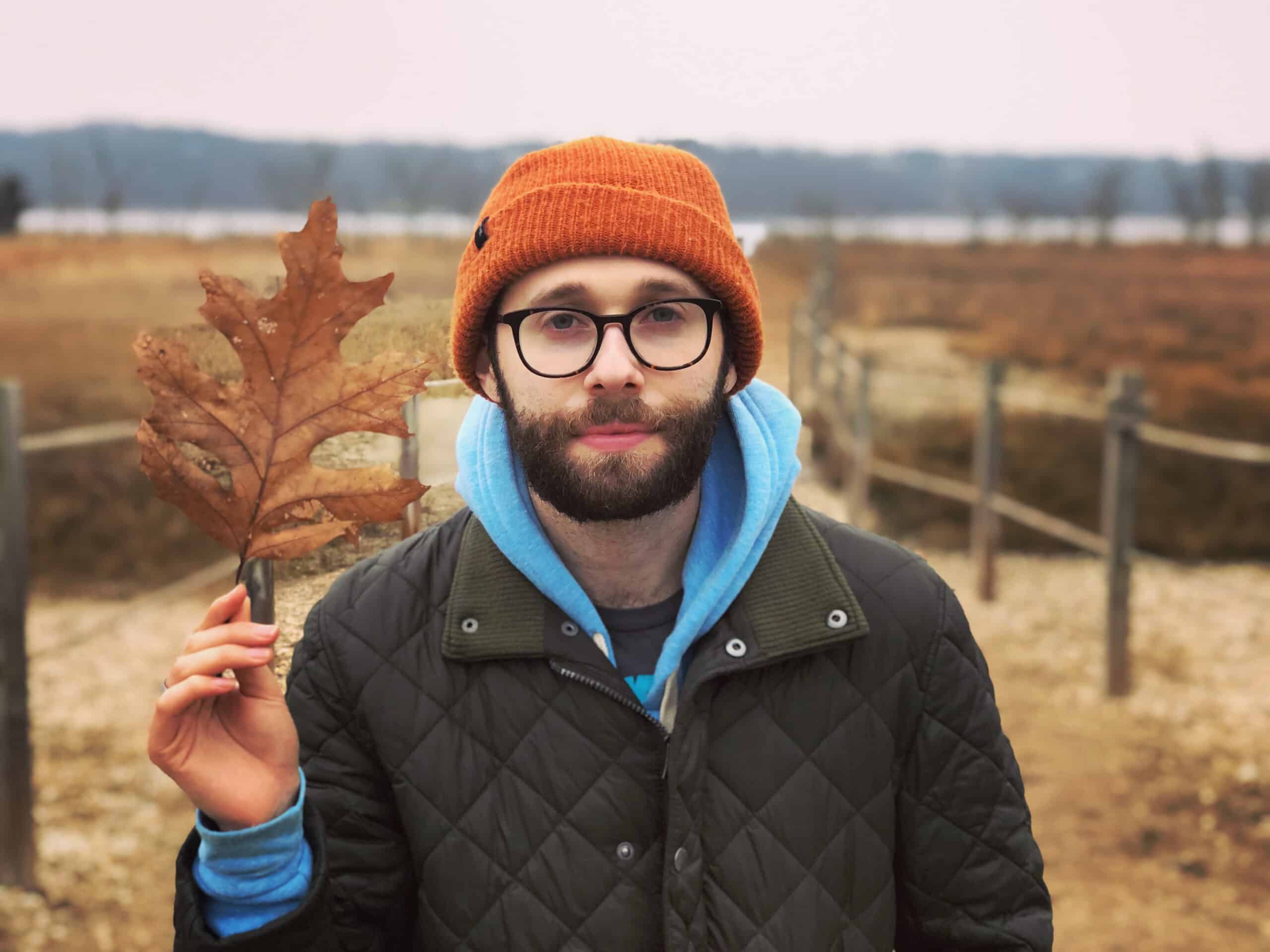 Ben Romano, dressed for cold weather, holds up a big autumn leaf. 