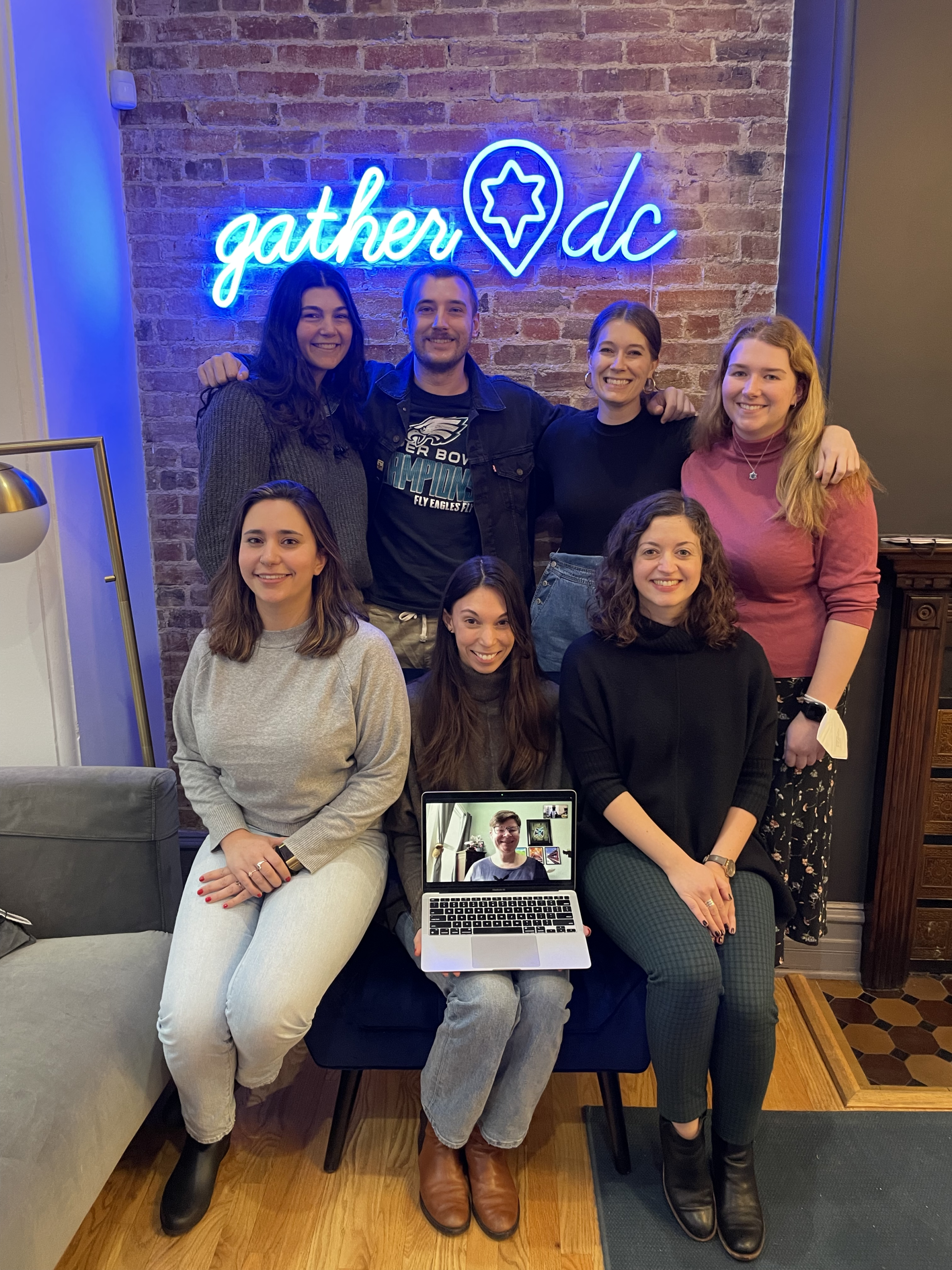 The GatherDC team poses in our townhouse living room in front of a neon GatherDC sign. 