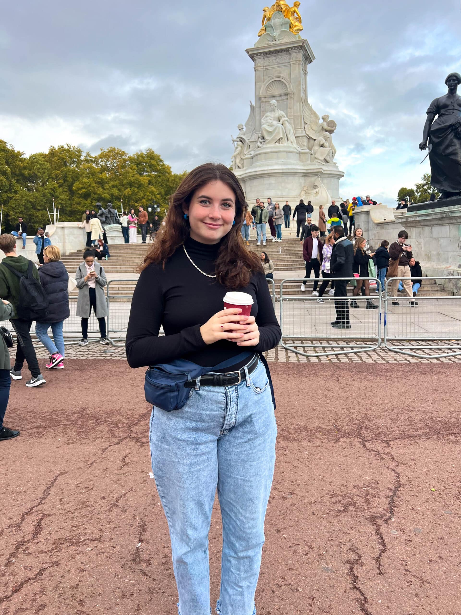 Mary outside Buckingham Palace, holding a coffee. 