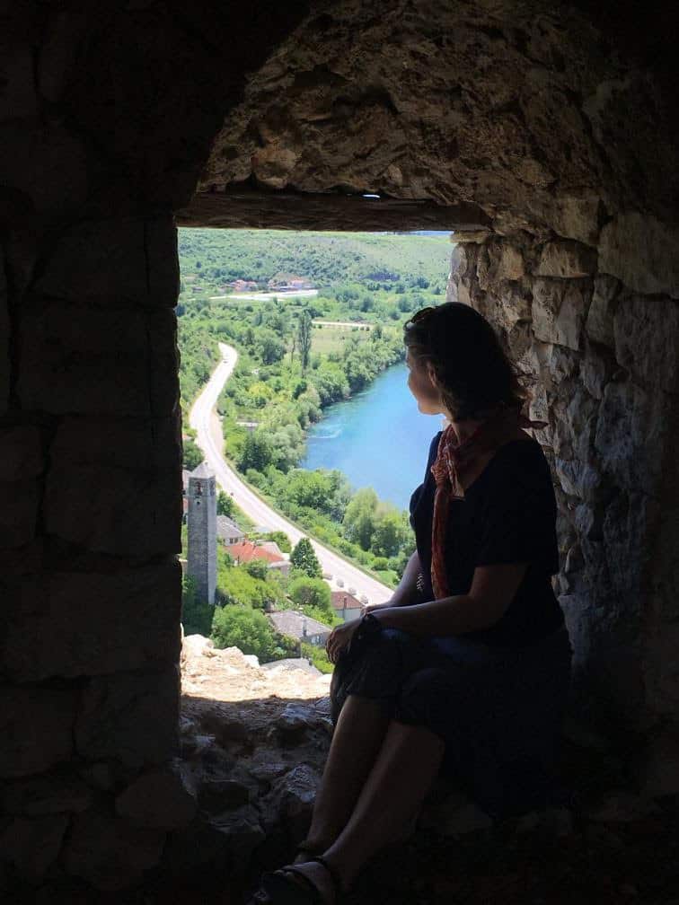 Amelia sits in a stone window overlooking a body of water. 