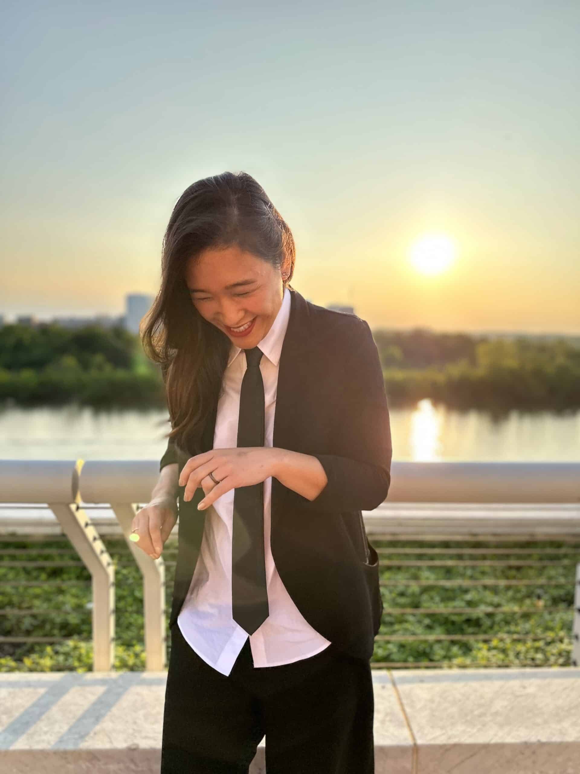 Liz in a suit and tie next to the river at sunset. 