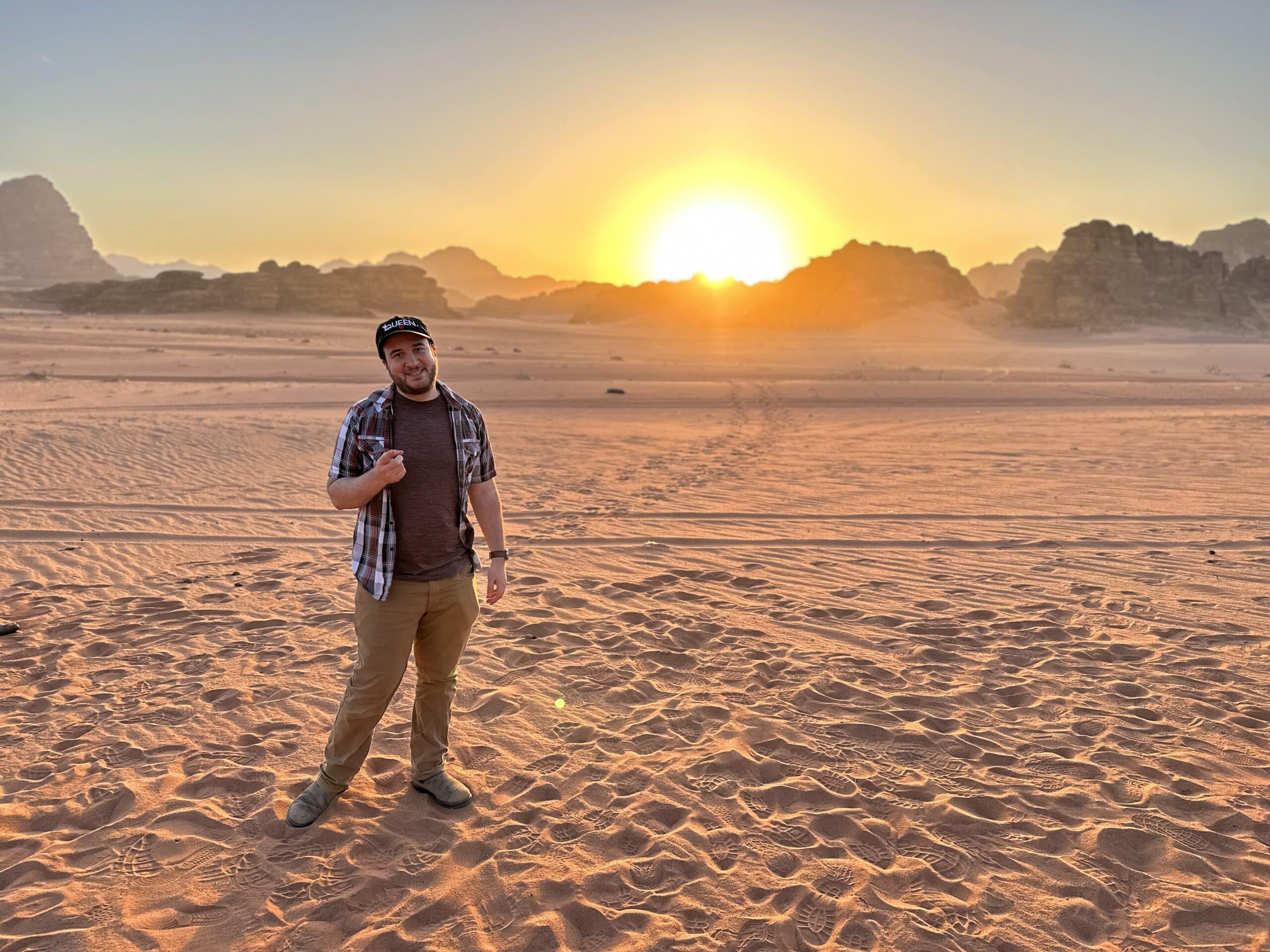 Josh stands in the desert, a sunset behind him.