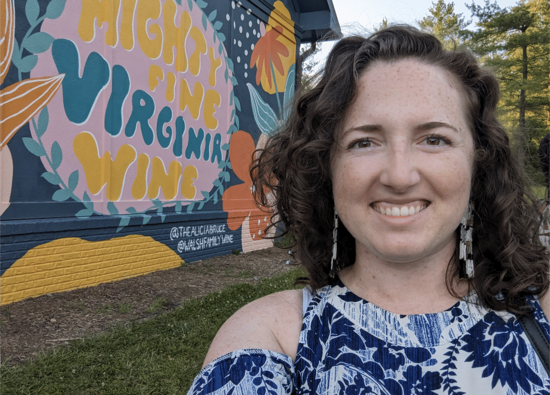 Rachel in front of a mural that says "Mighty Fine Virginia Wine"