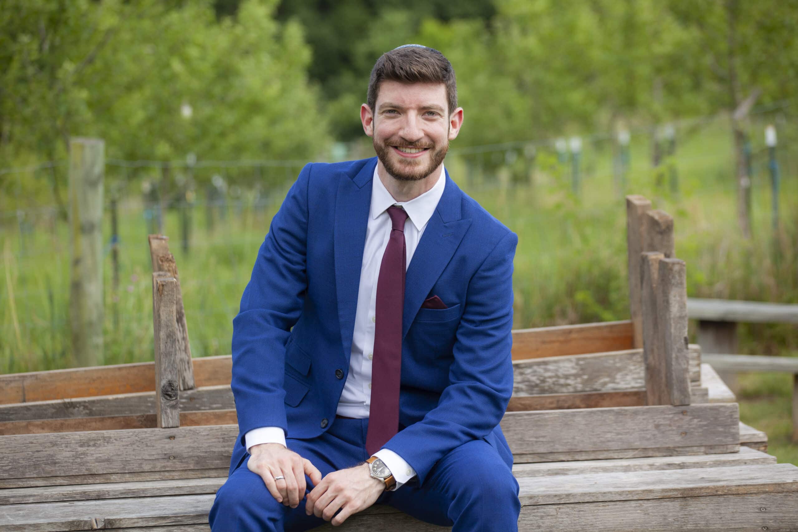 Marc in a blue suit on a wooden bench. 