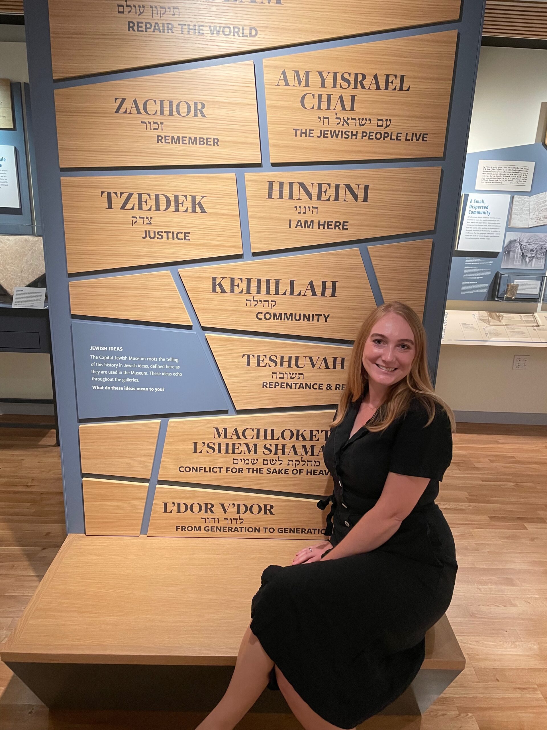Kelsey sits in front of a display of Jewish tenets, in Hebrew and English translations. 