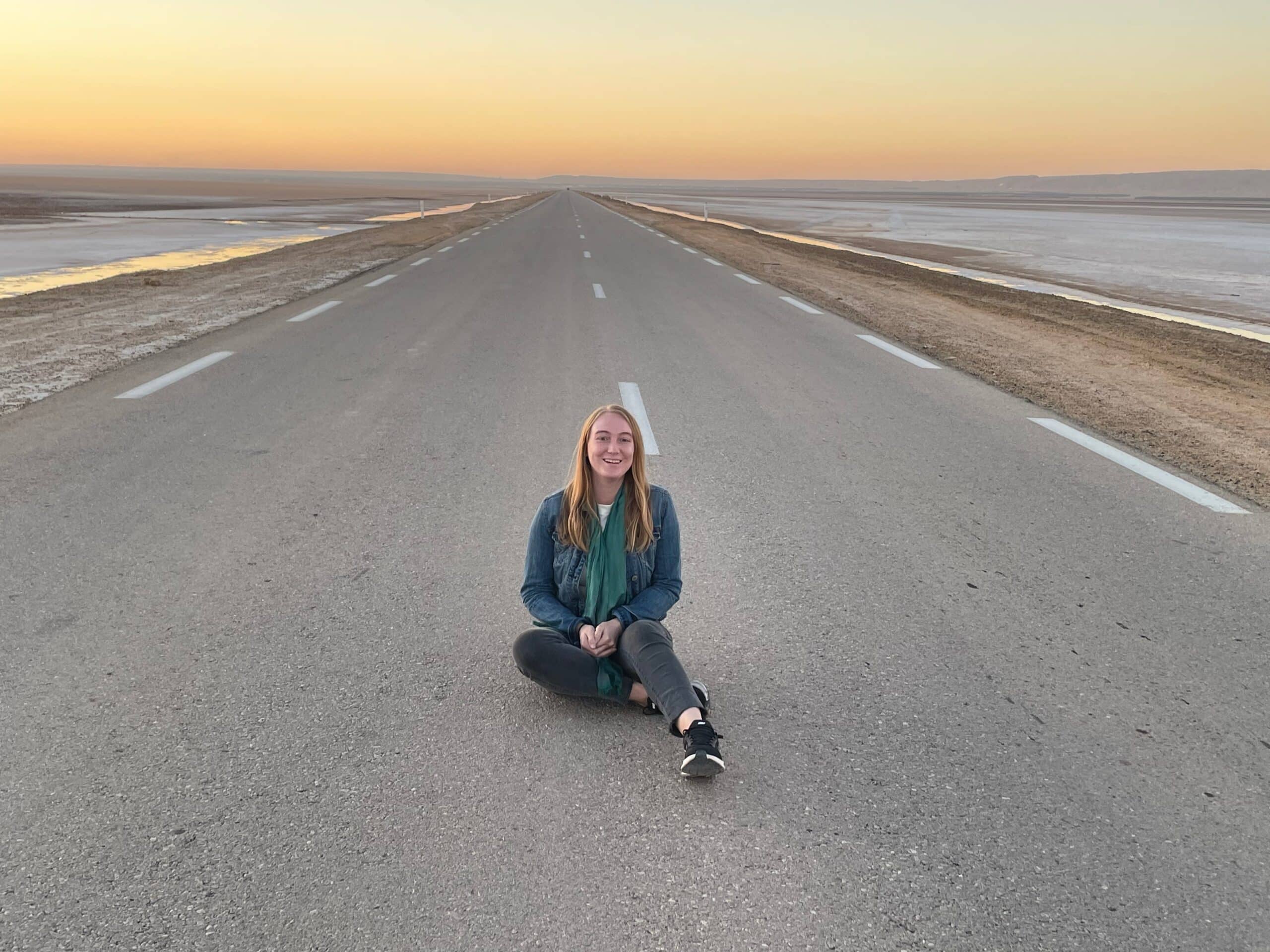 Kelsey sits in the middle of a road at sunset. 