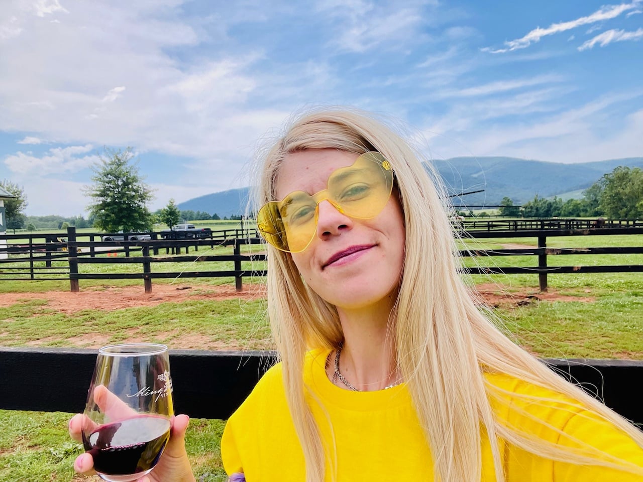 Rachel with a glass of wine and yellow sunglasses on a farm.
