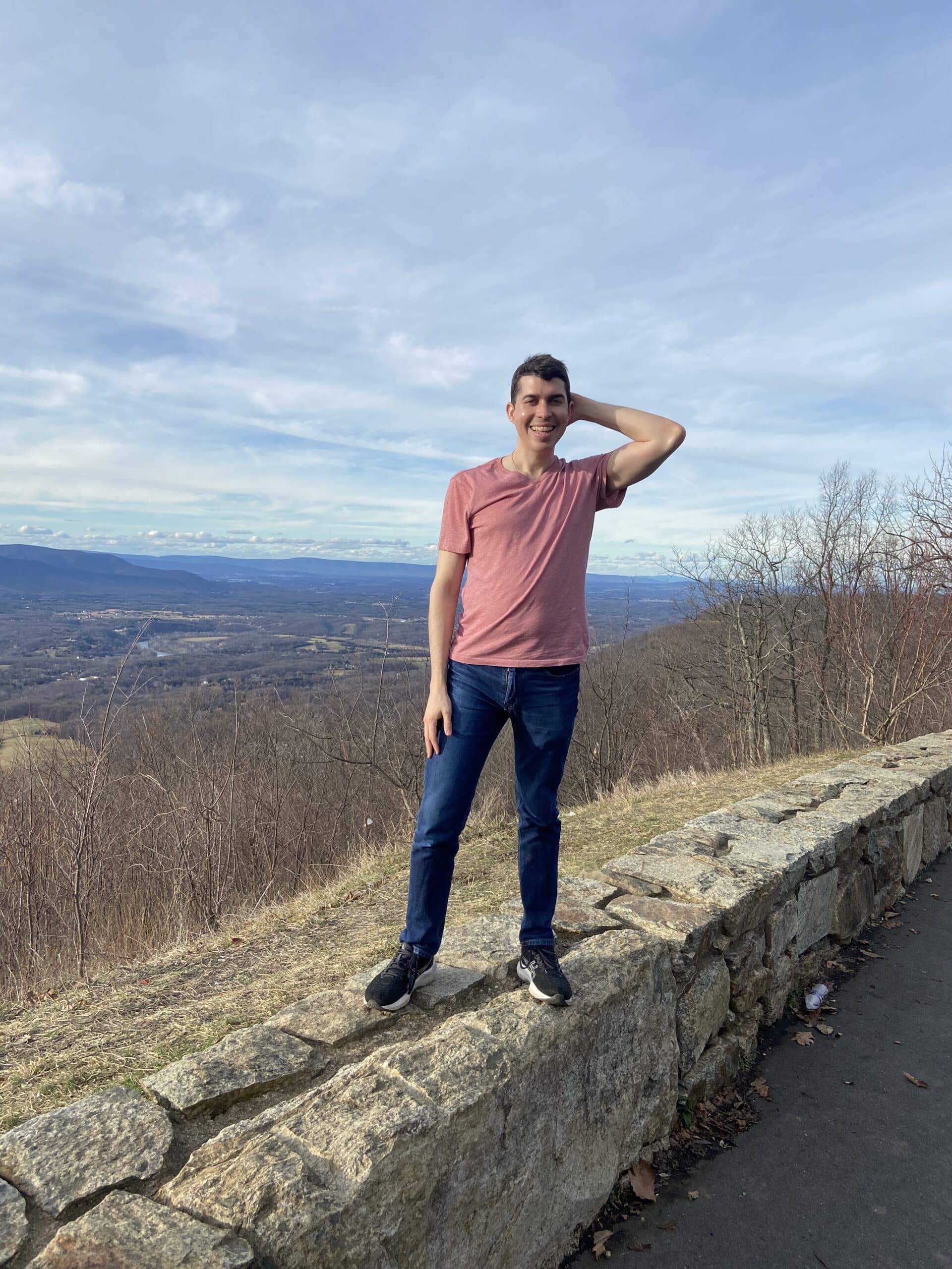 Alejandro stands on a low stone wall with a wooded background.