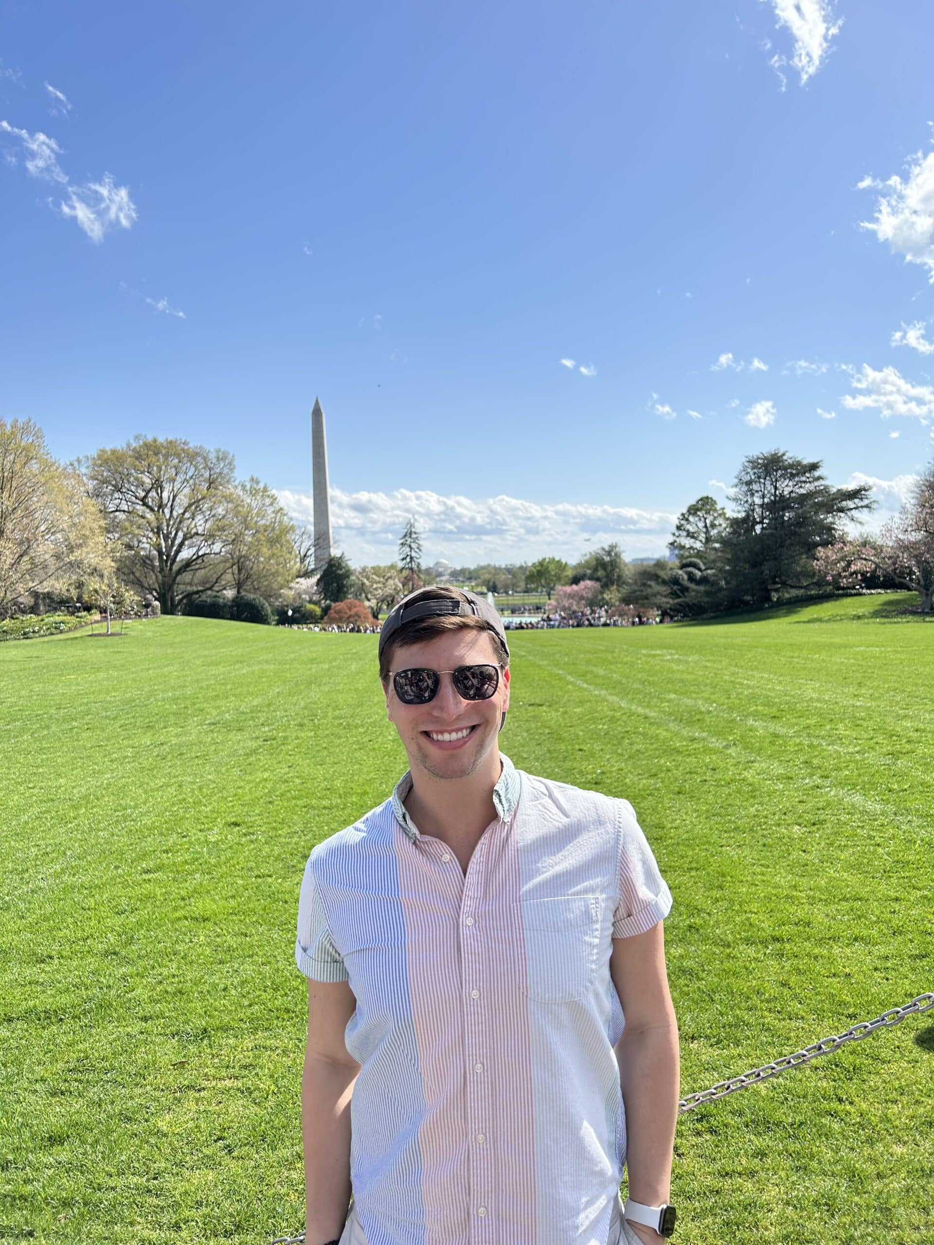 Aaron stands in a open green space, wearing sunglasses. 