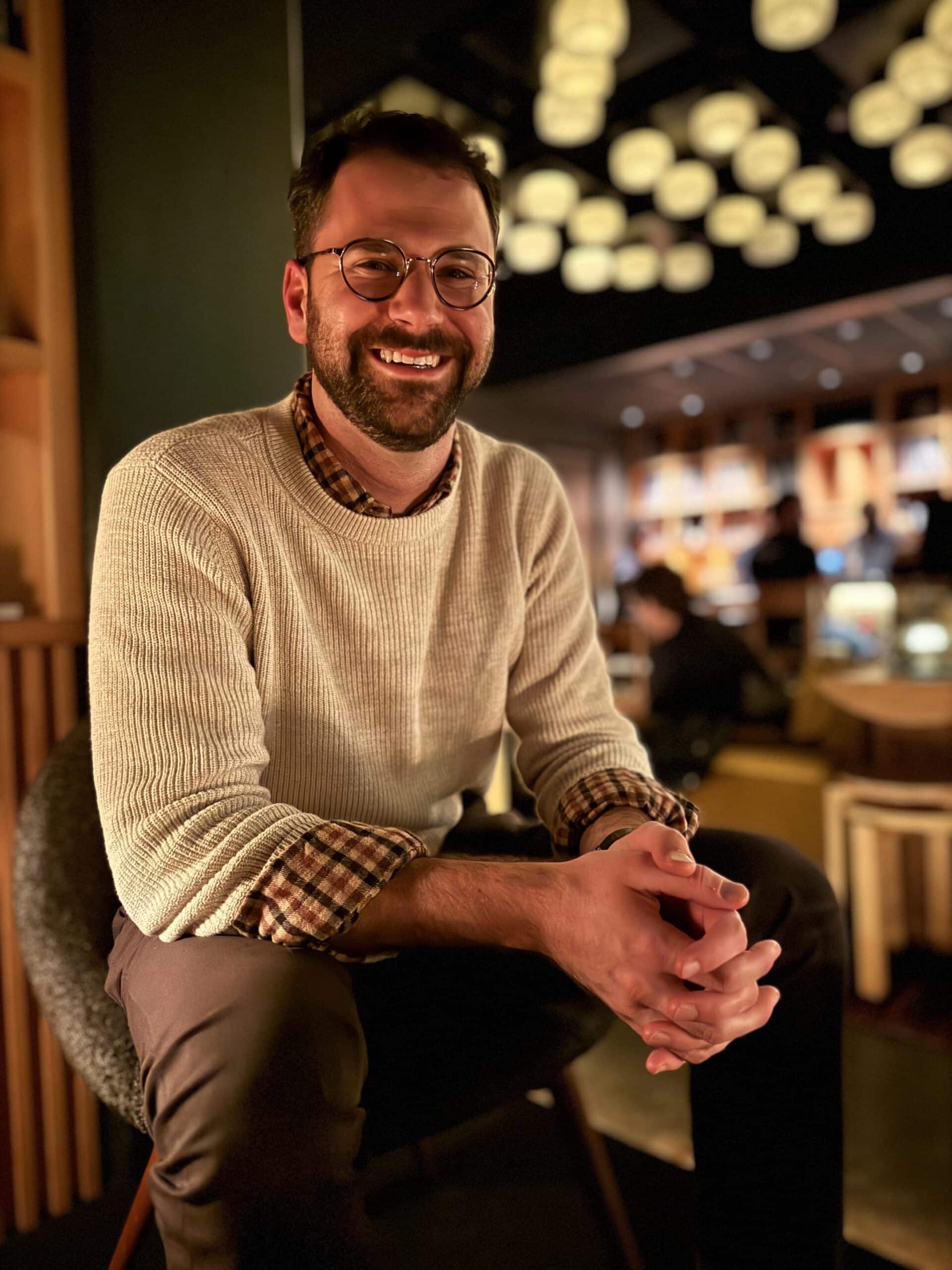 Ben smiling, wearing a sweater indoors. 