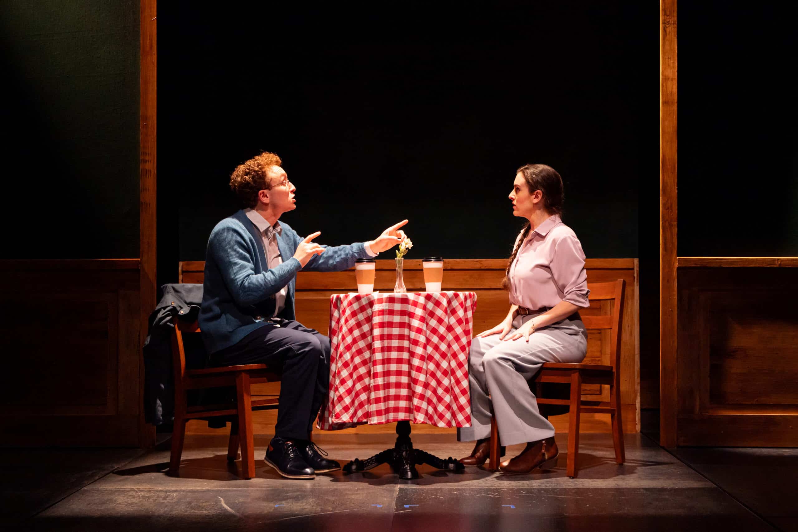 Ethan onstage at a table with another actor. 