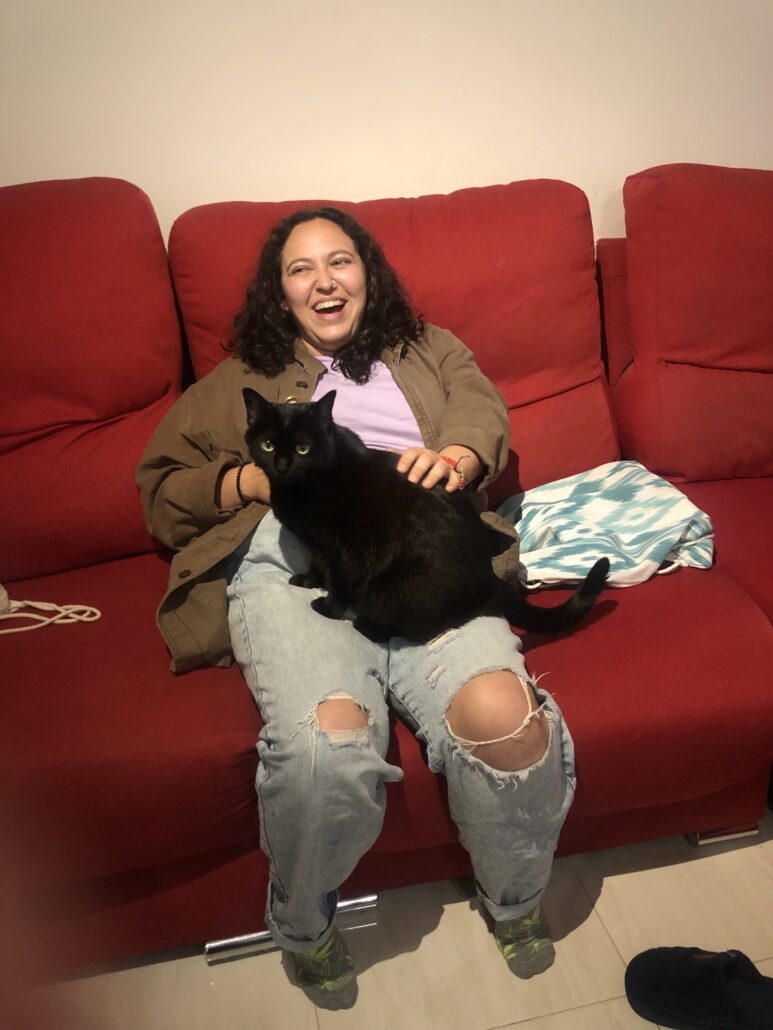 Heather and her cat sit on a red couch. 