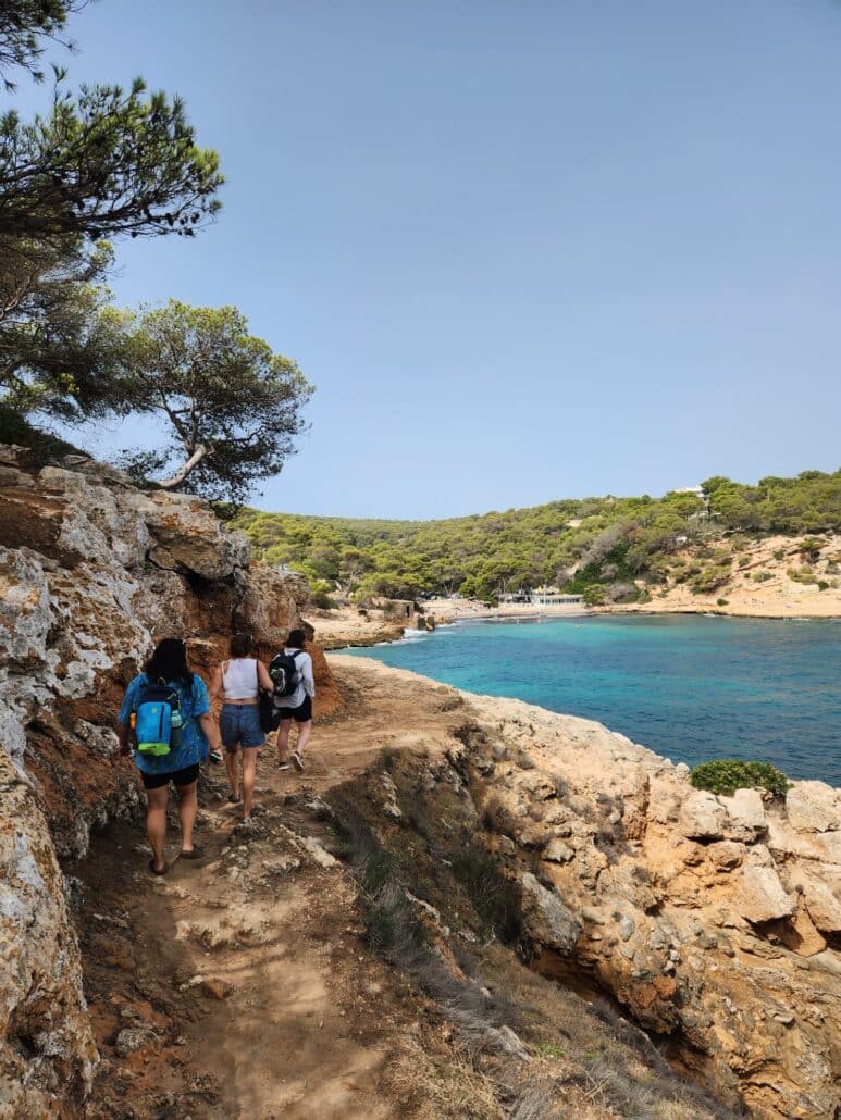 Three people hike on a rocky coastline. 