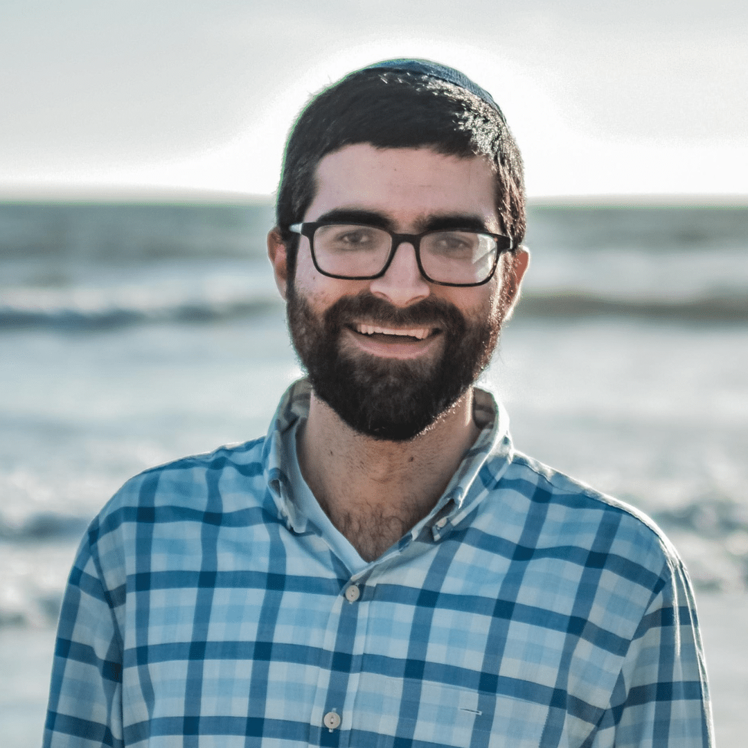 A bearded man in a blue shirt on the beach.