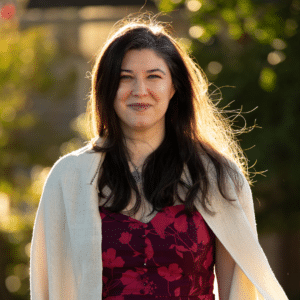 A white woman in a floral dress and cardigan at sunset.