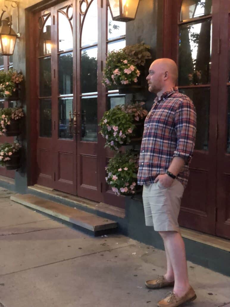 Richard in front of a restaurant in a button down shirt and boat shoes.