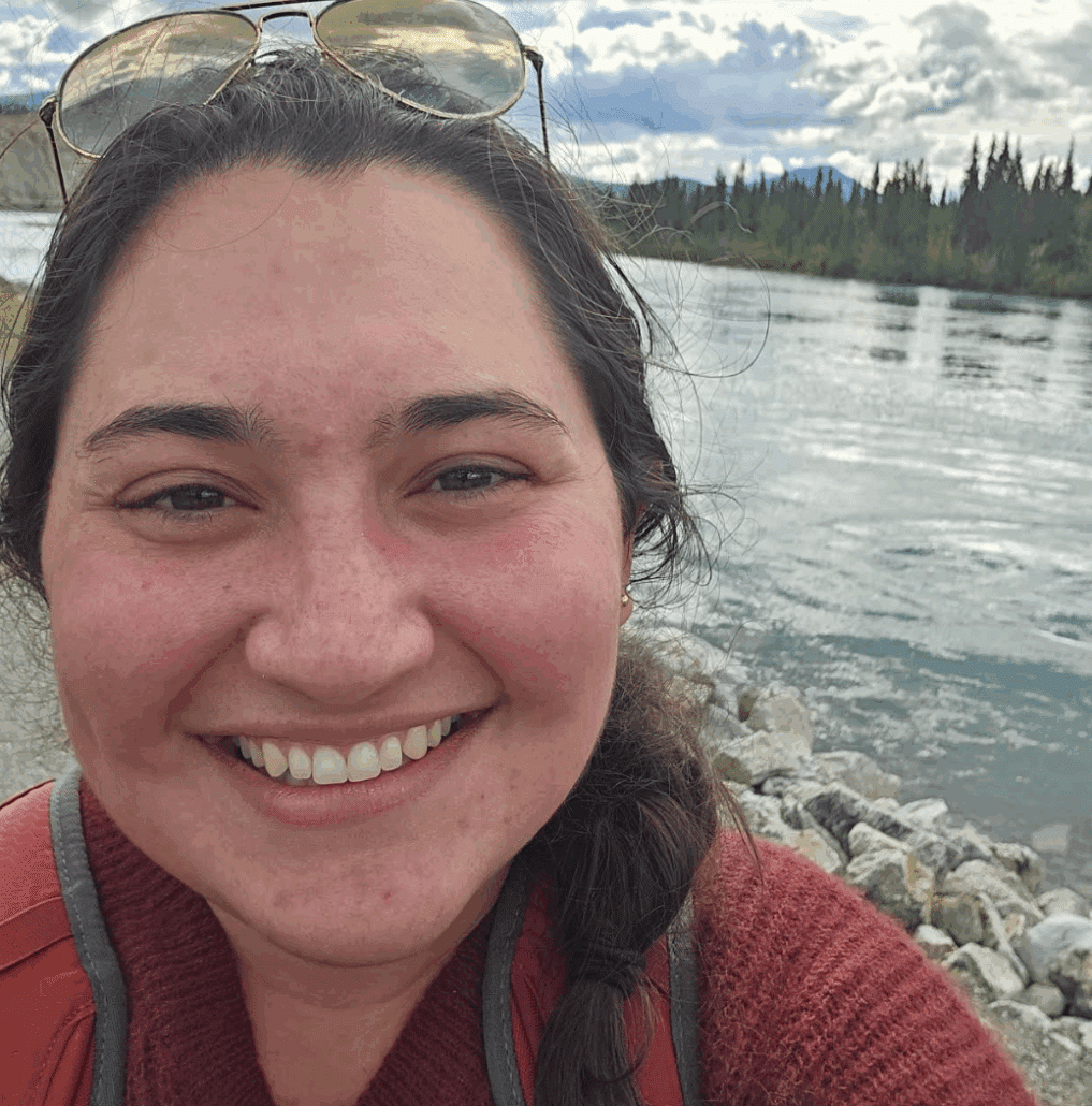 Emma takes a selfie from the shoreline of a river.