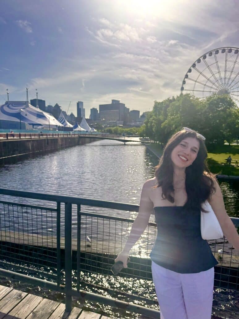 Hannah stands on a bridge with a ferris wheel behind.