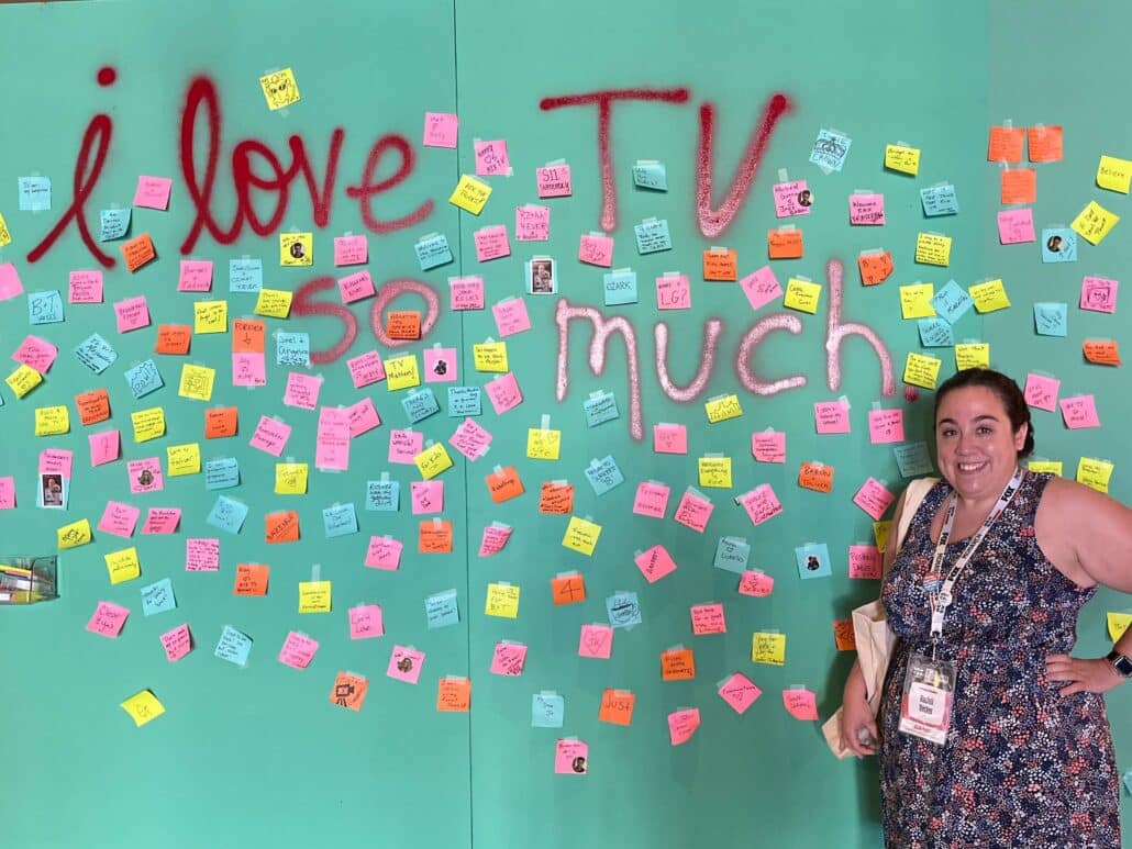 Rachel in front of a green wall reading "i love tv so much"