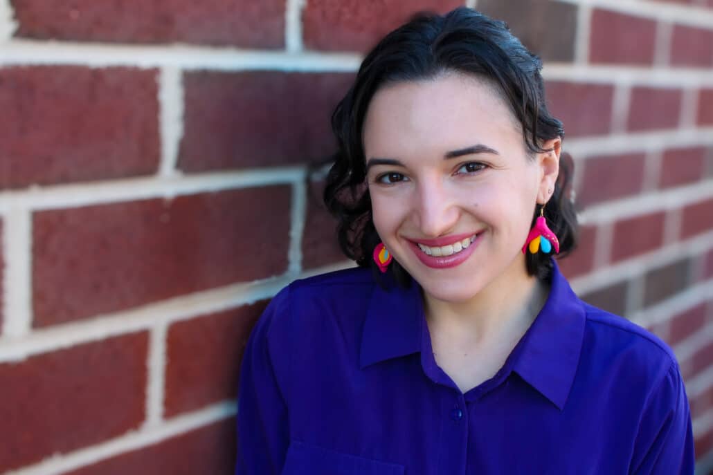 Miriam in a blue shirt against a brick wall.