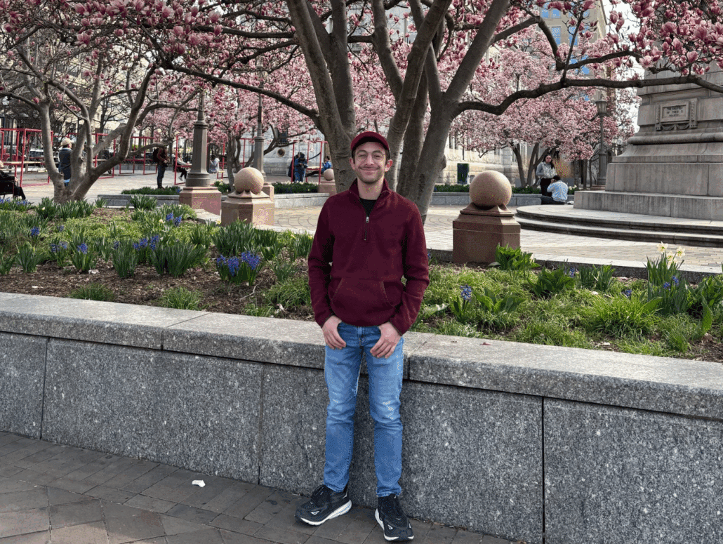 Noah under cherry blossoms in a red sweater.