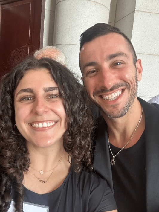 Maya takes a selfie with a man in a dark jacket.