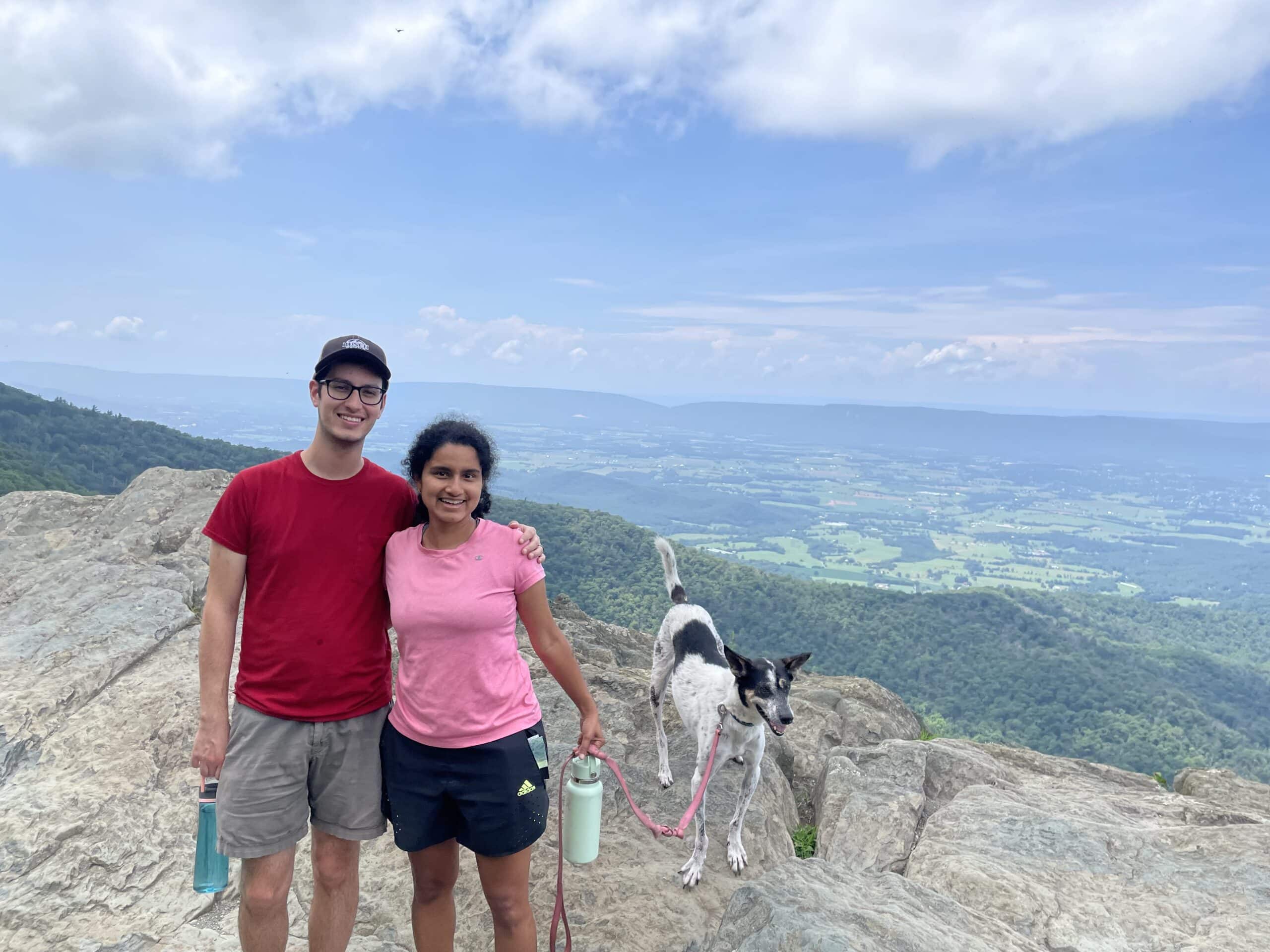 Sam and a woman in a pink shirt and a dog on a hilltop.